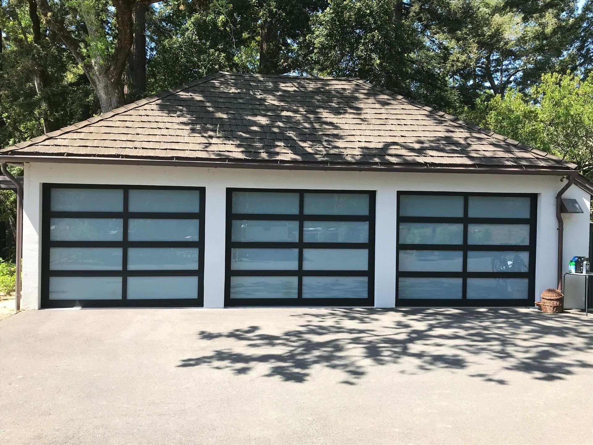 Three-car garage with frosted glass doors under a shingled roof, surrounded by trees and sunlight.