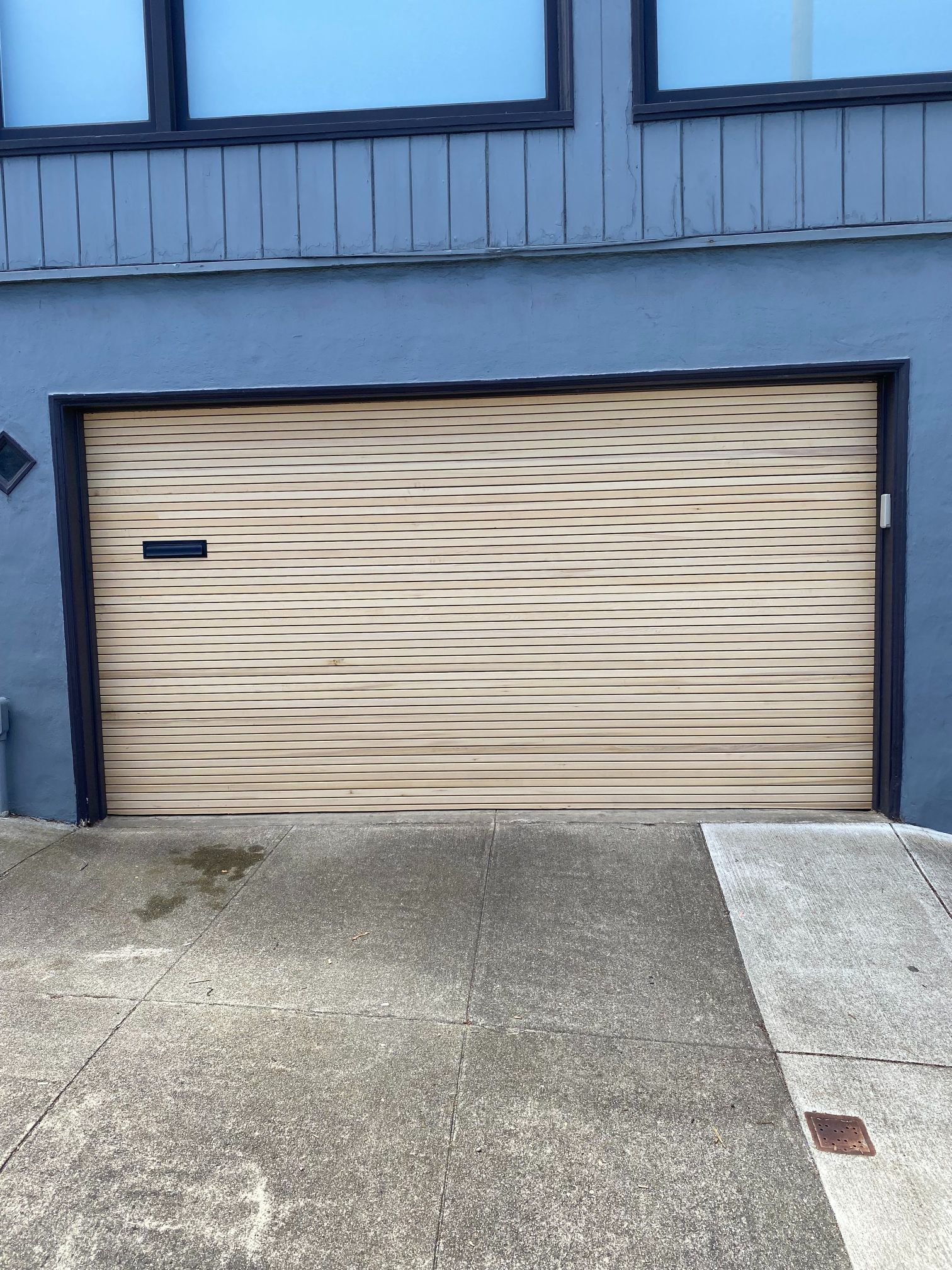 Beige roll-up garage door on a gray building with a concrete driveway.