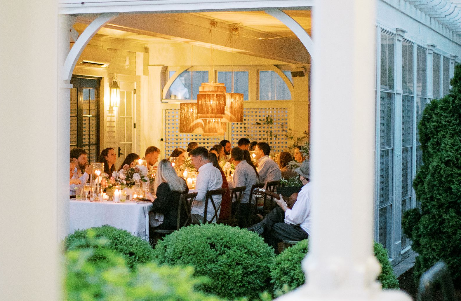 Group of women posing outside a white building with large windows, smiling, some seated on a white bench.