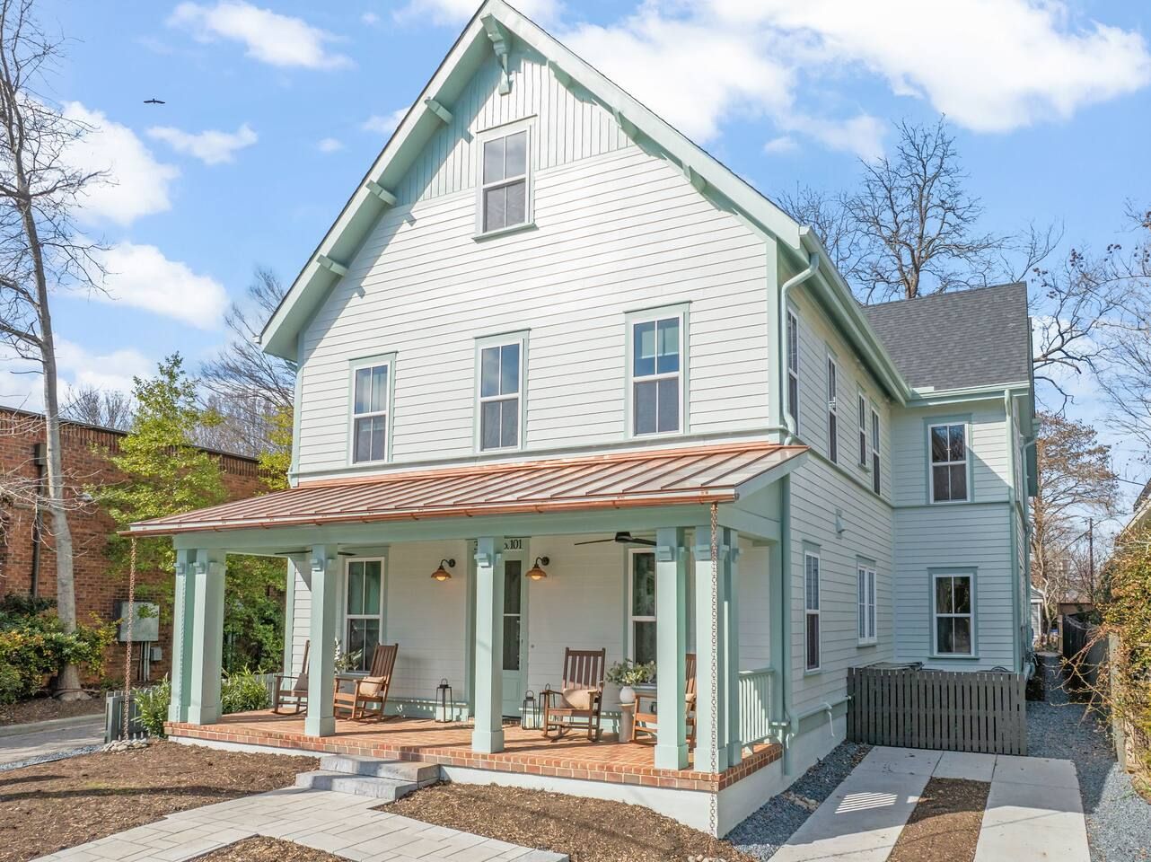 A light blue two-story house with a copper-roofed porch, shuttered windows, and a front yard with a stone walkway.