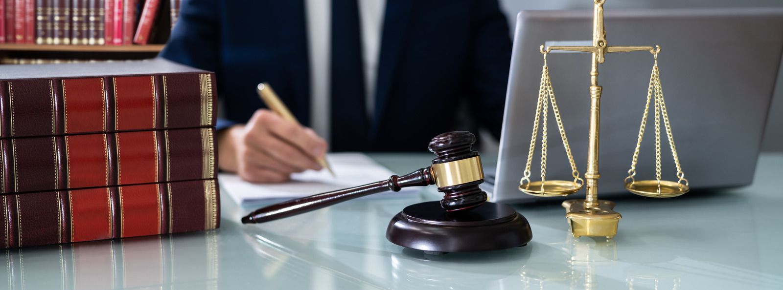 A judge is writing on a piece of paper next to a gavel and scales of justice.