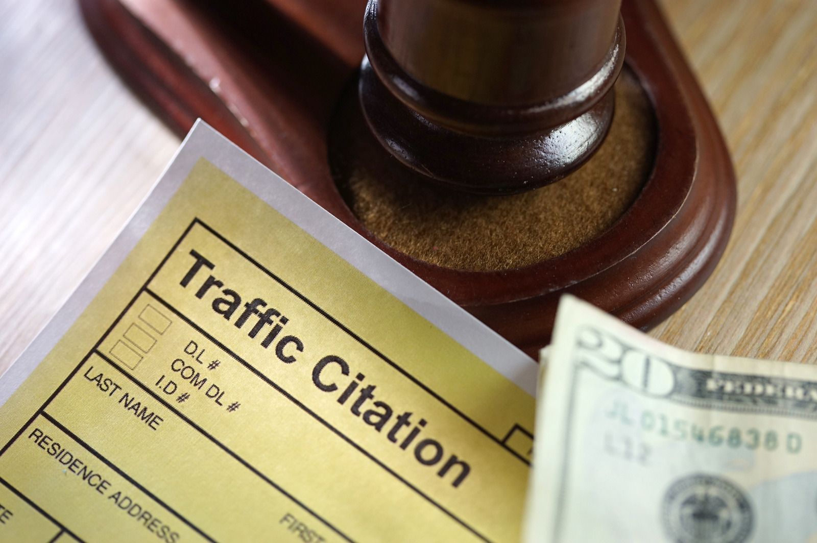 Traffic citation, gavel, and twenty-dollar bill on wooden surface, suggesting a fine.