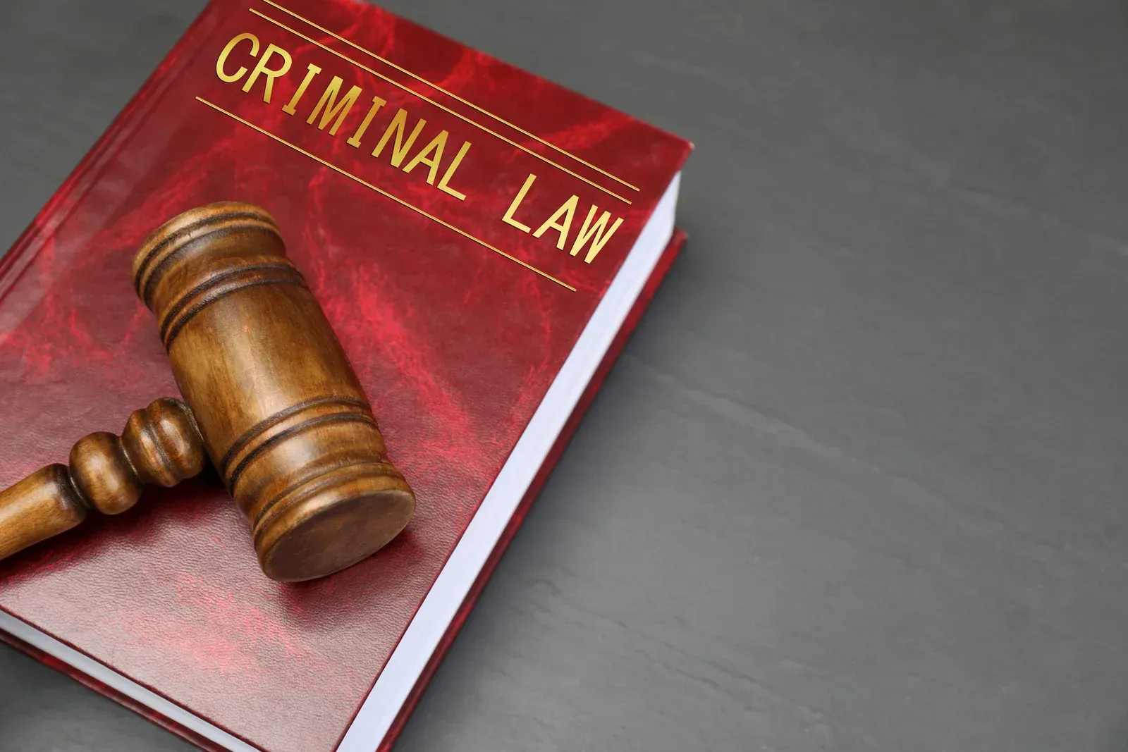 Wooden gavel resting on a red Criminal Law book on a gray surface.