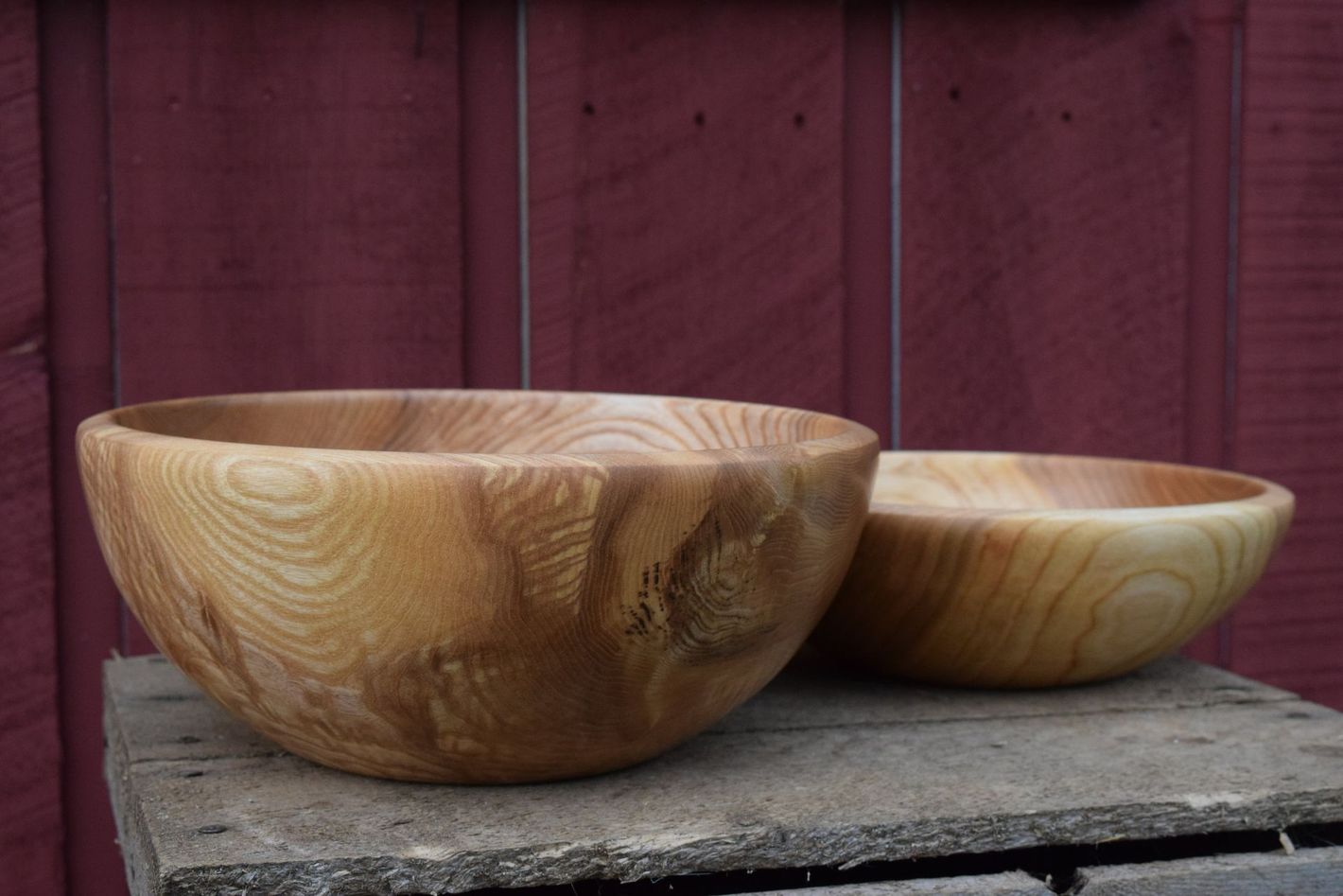 Two hand-turned wooden bowls sitting on a wooden table in front of a red wall.