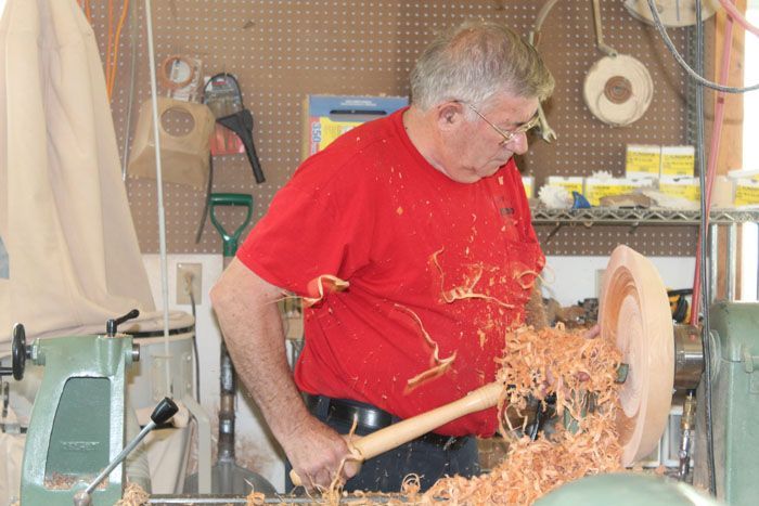 A man in a red shirt is working on a wood lathe turning a wooden bowl.