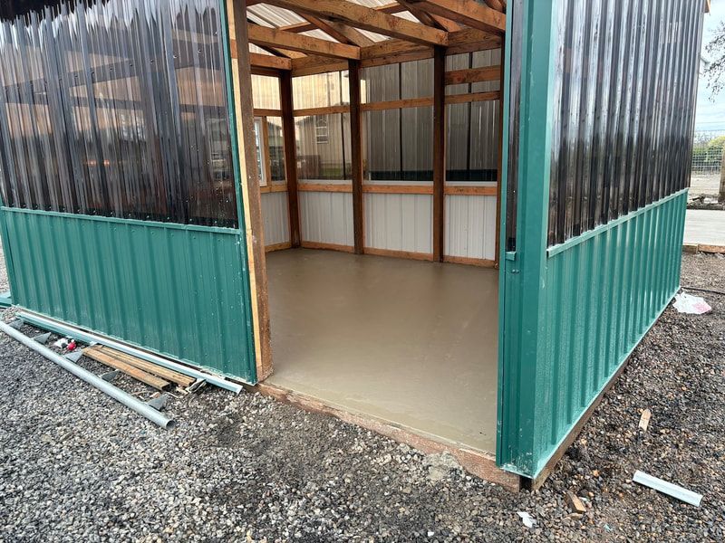 A green shed with a wooden roof is sitting on top of a gravel lot.