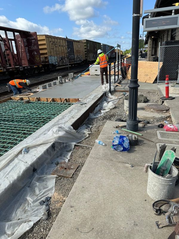 A group of construction workers are working on a sidewalk next to a train track.