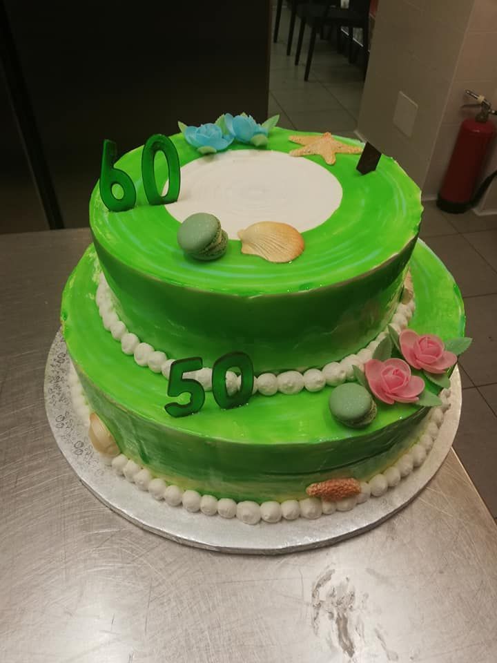 Torta verde a due piani decorata con macaron, fiori e numeri 50 e 60.