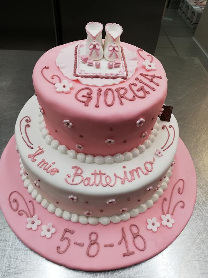 Torta per battesimo a due piani rosa e bianca con decorazioni a forma di scarpine per neonati, il nome