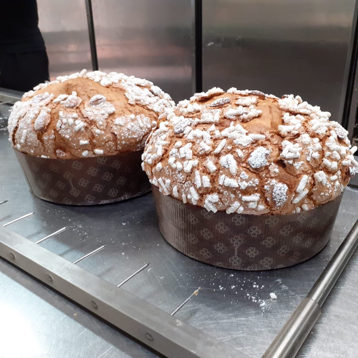 Due panettoni rotondi con glassa di zucchero cristallizzato, su un vassoio di metallo.