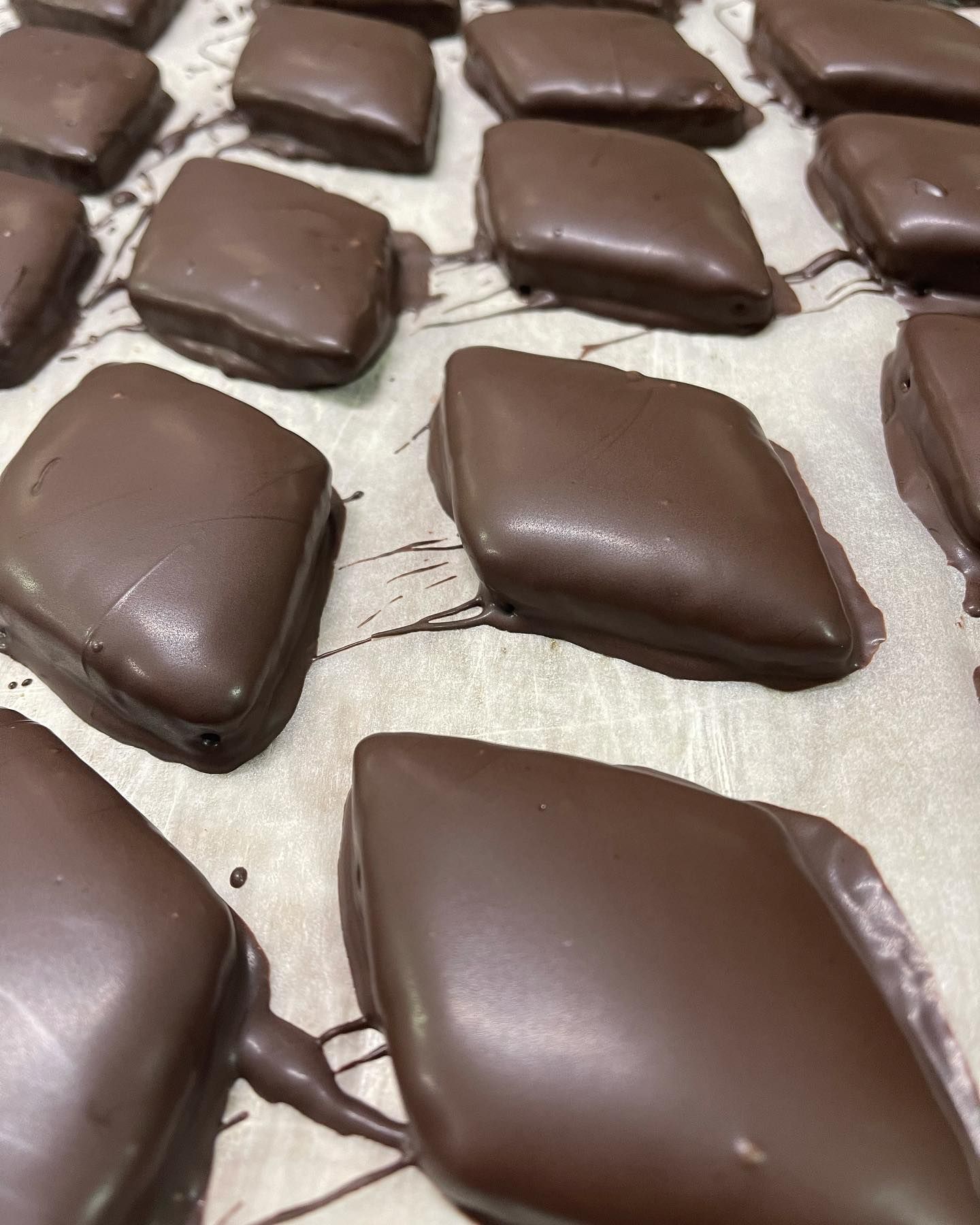 Caramelle a forma di diamante ricoperte di cioccolato su carta da forno; rivestimento marrone scuro con qualche goccia.