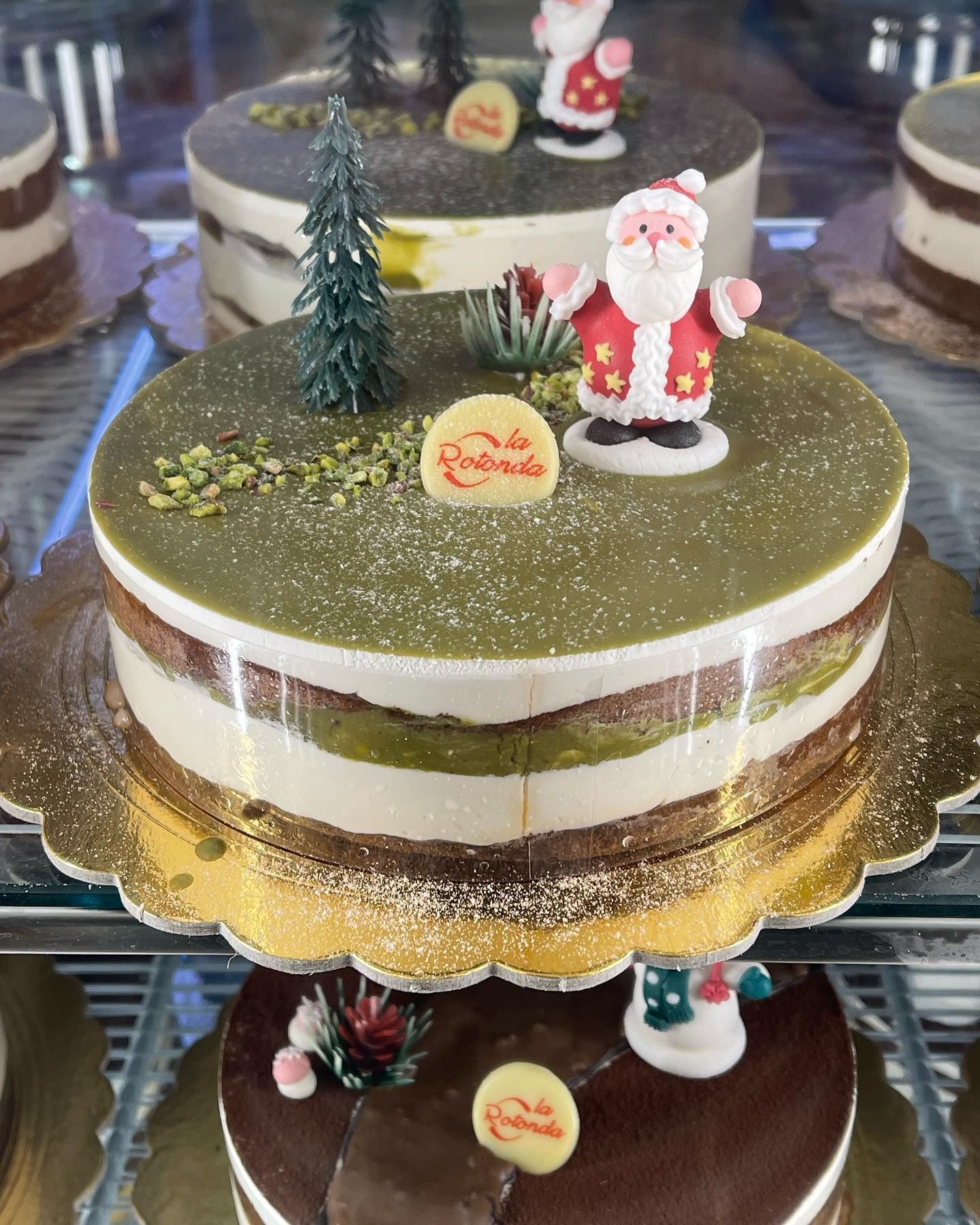 Torta natalizia con glassa verde, strati, statuetta di Babbo Natale e albero decorativo.