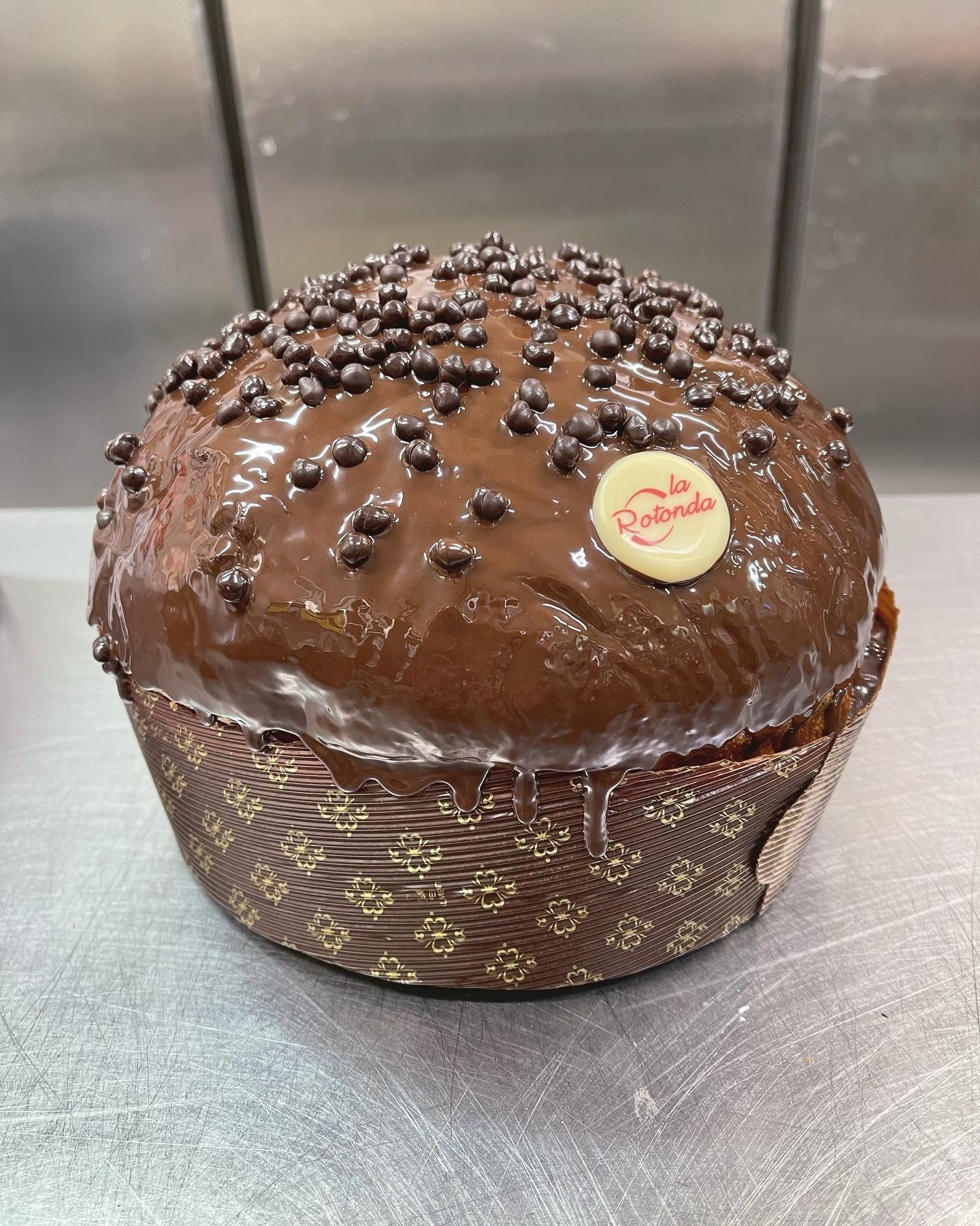 Prodotto da forno ricoperto di cioccolato con granella scura, in un pirottino di carta e con un logo sulla parte superiore.