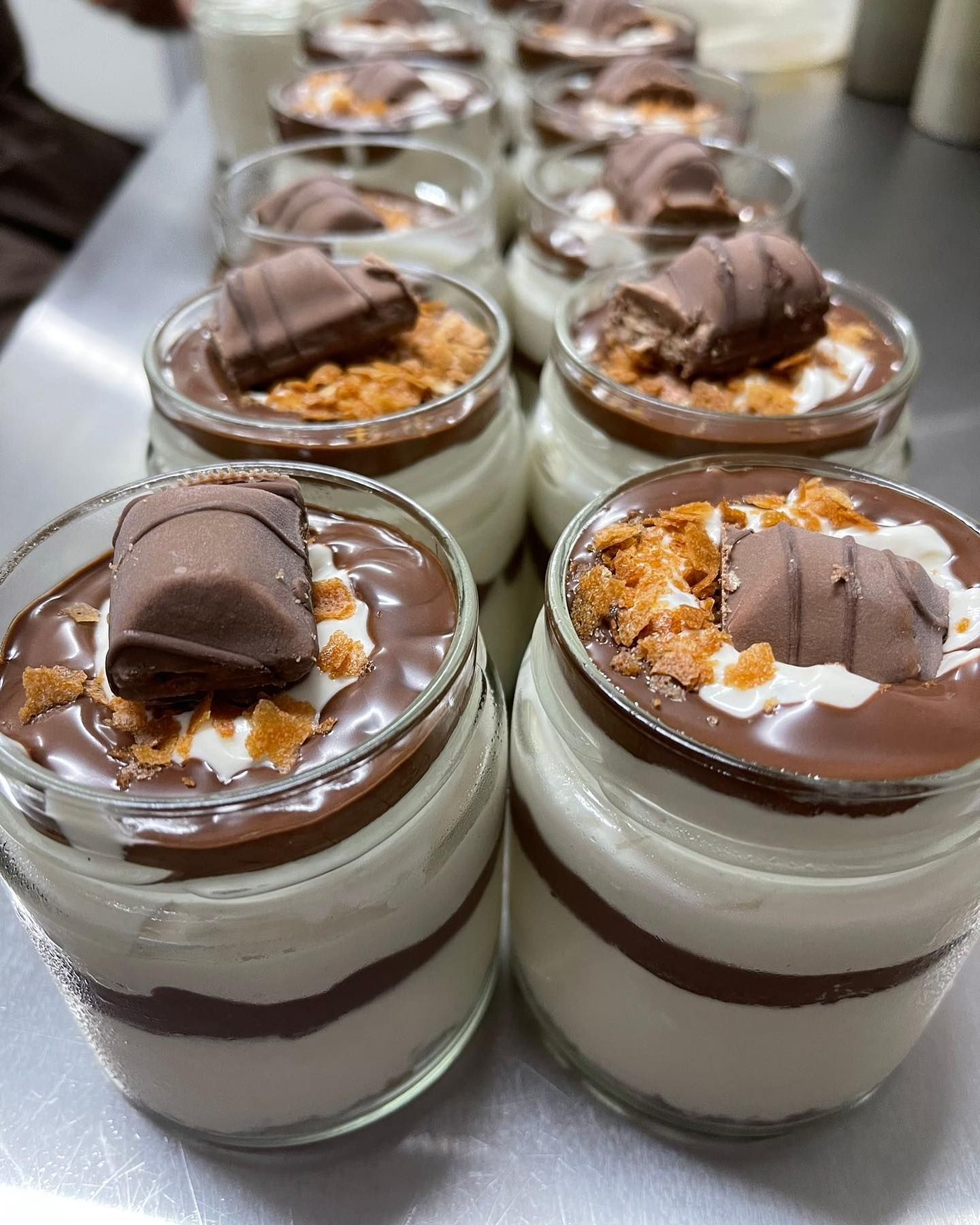 Barattoli di vetro con dessert a strati ricoperti di salsa al cioccolato, briciole di biscotti e una barretta Kinder Bueno.