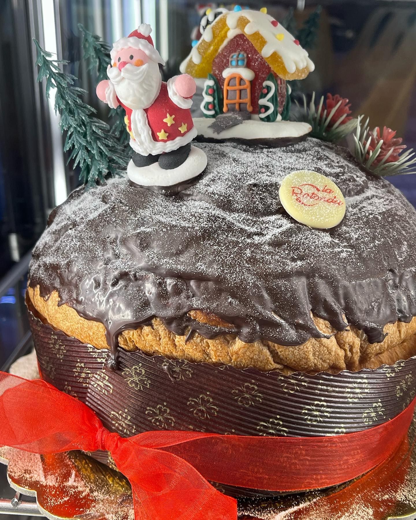Panettone natalizio, glassato al cioccolato, decorato con la figura di Babbo Natale e la casetta di pan di zenzero.