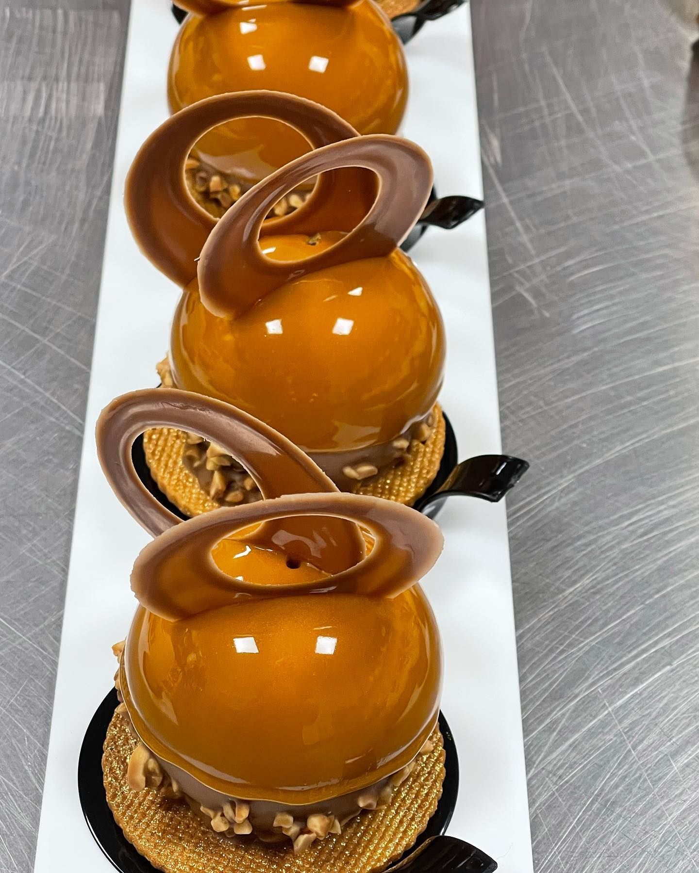 Quattro dessert al caramello glassati su un vassoio bianco, ognuno con un anello di cioccolato e una base di biscotto.