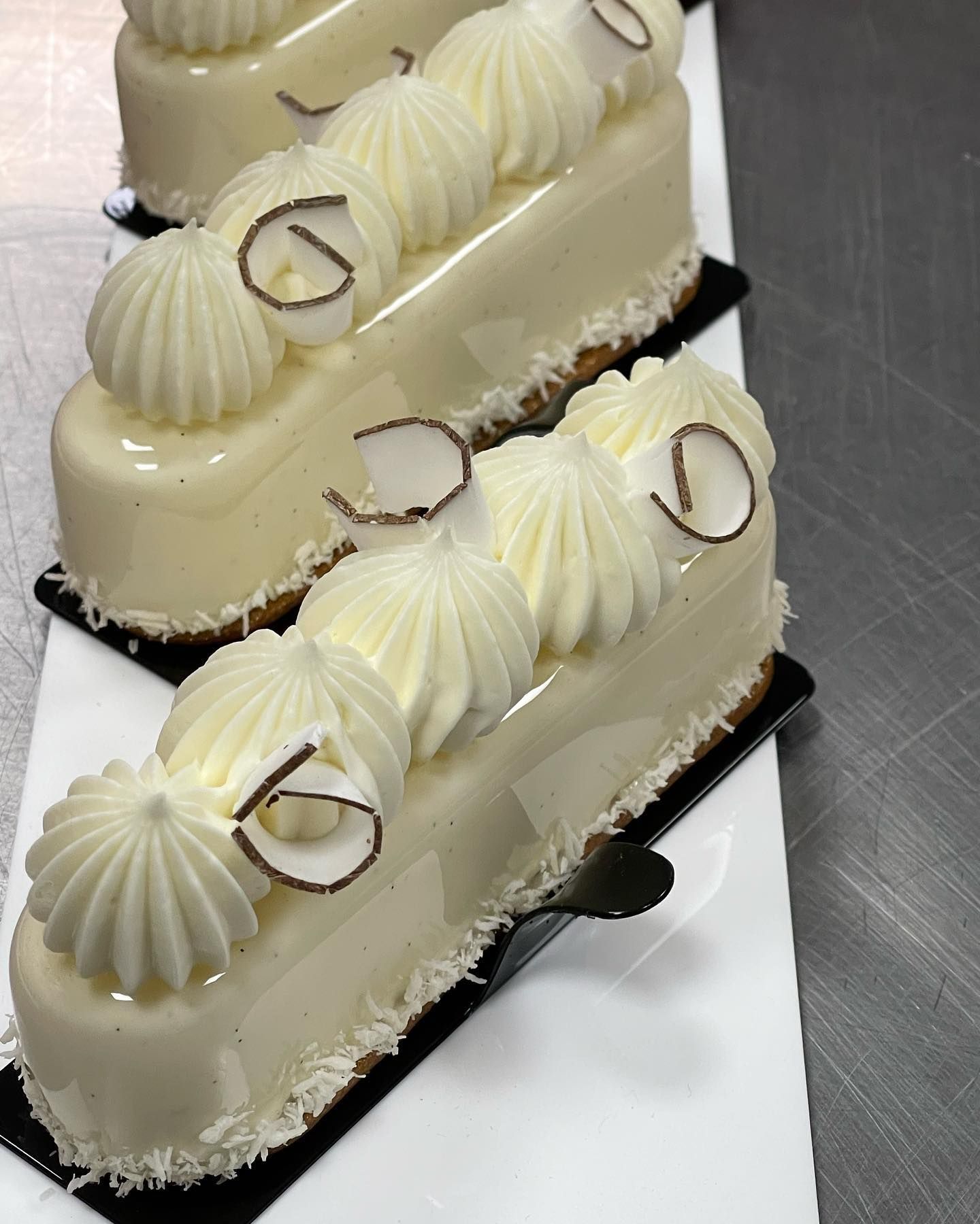 Pasticcini rettangolari glassati di bianco, ricoperti di panna montata e scaglie di cocco.