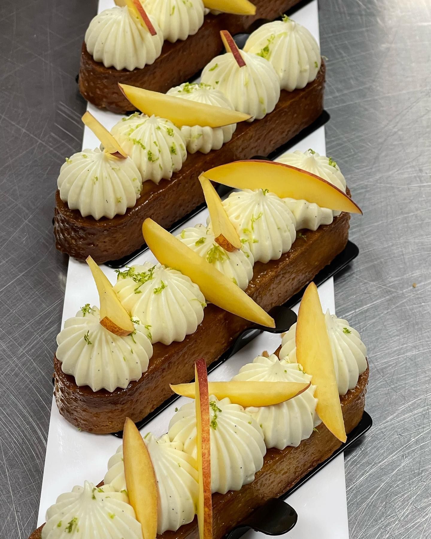 Pasticcini rettangolari ricoperti di crema bianca, fette di pesca e scorza di lime.