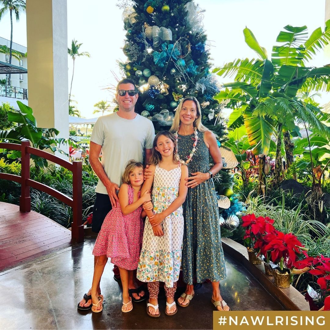 A family of four smiles in front of a decorated tree.