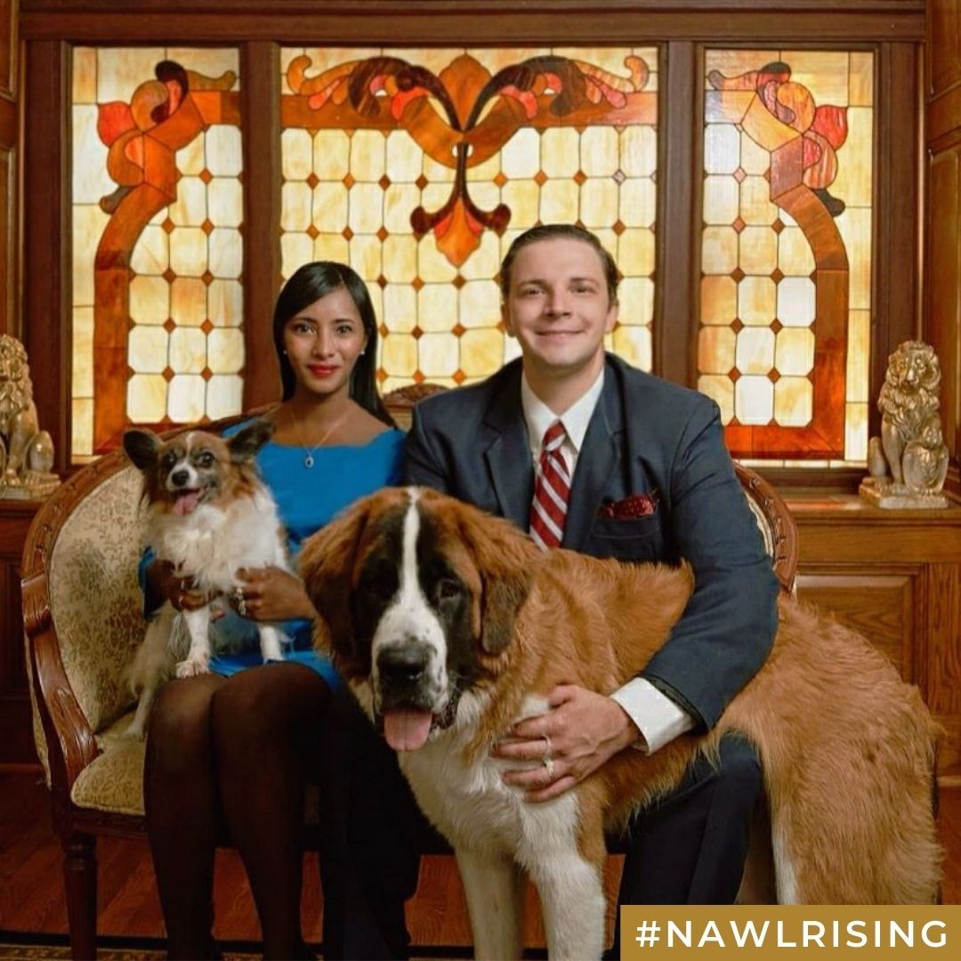 A couple sits with their dogs in front of a stained glass window.