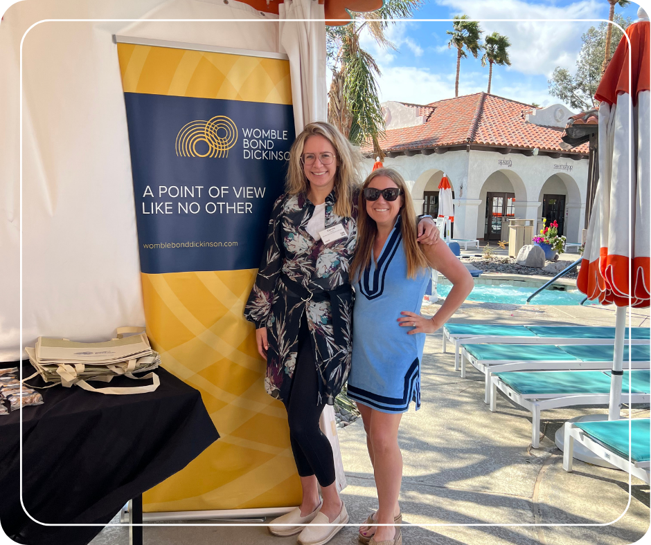 Two women standing next to a pop-up banner with sponsor logo next to a pool.
