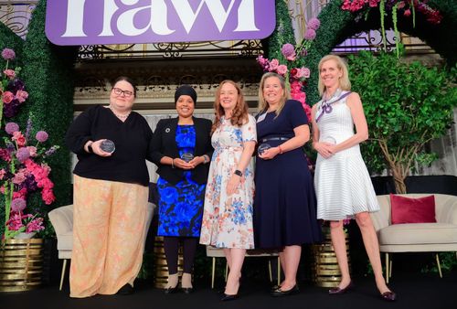Members holding awards on a stage in front of a backdrop with NAWL's logo.