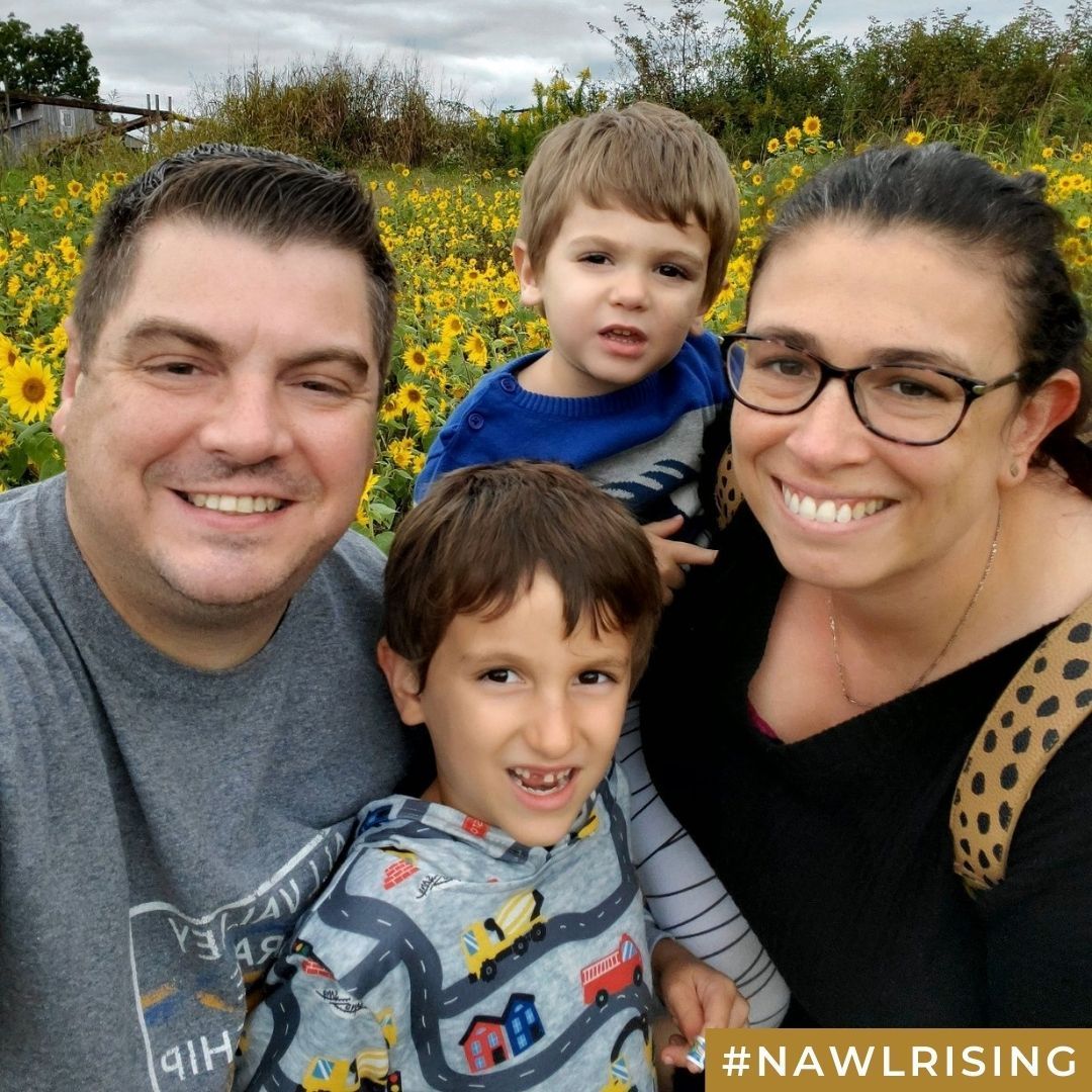 A family of four smiles together in front of a field of sunflowers.