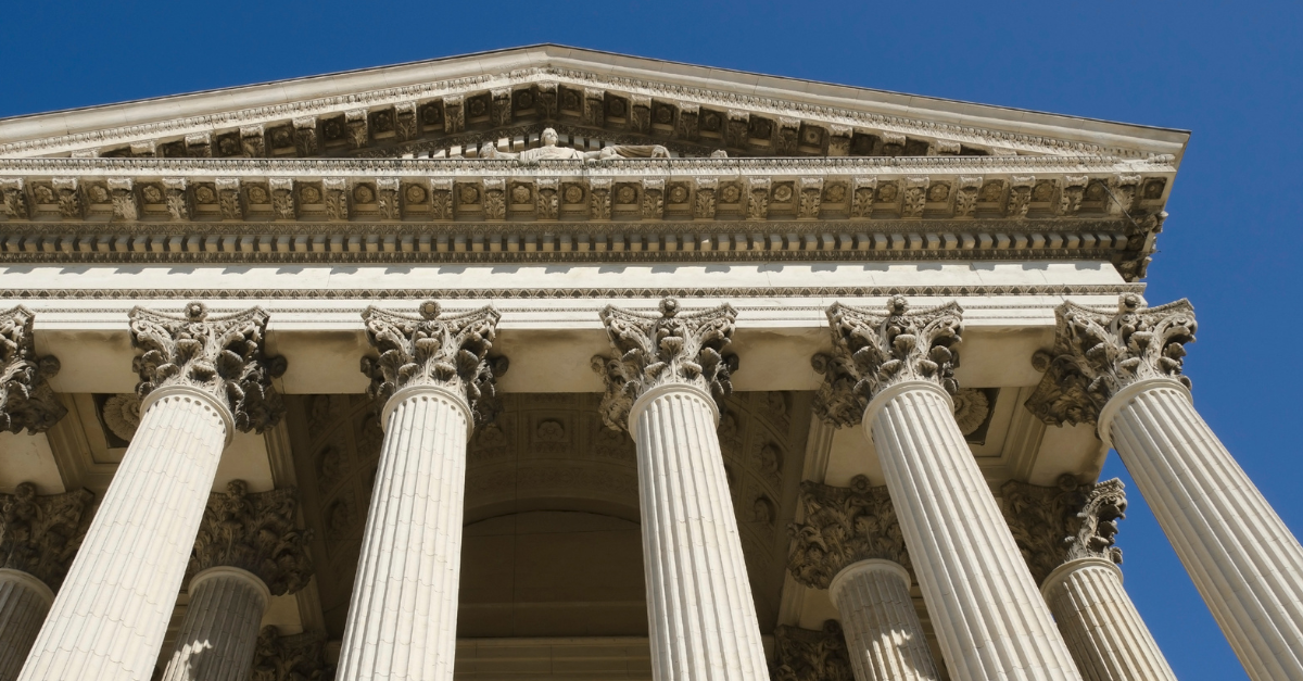 Columns of a classical building with ornate carvings against a clear blue sky.
