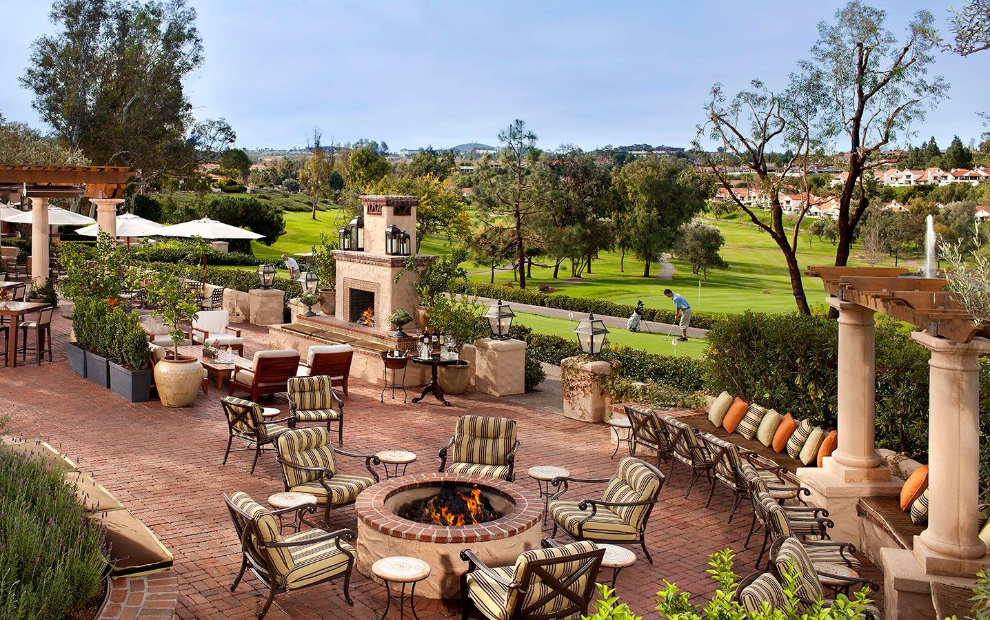 A patio with chairs and a fire pit next to a golf course.