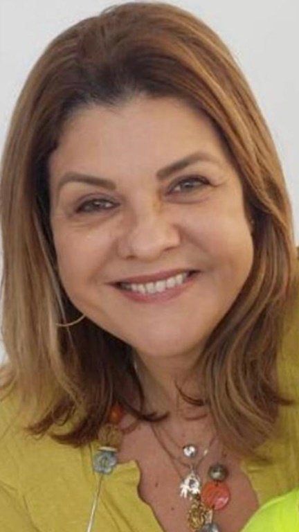 Uma mulher vestindo um suéter amarelo e um colar está sorrindo para a câmera.