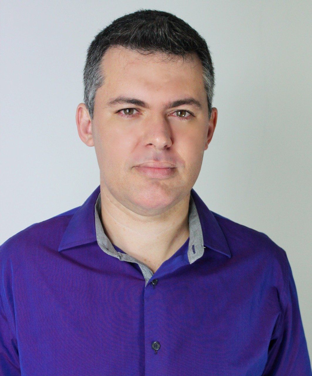 Um homem de camisa roxa está olhando para a câmera