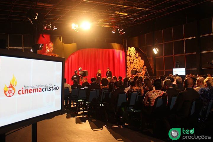 Um grupo de pessoas está sentado em frente a uma tela que diz cinemacristo