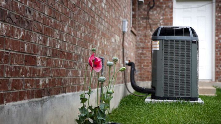 An air conditioner is sitting in the grass next to a brick wall.