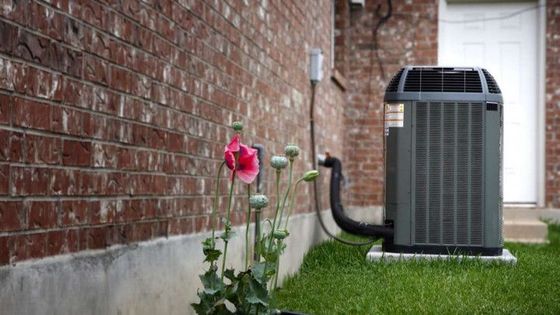 An air conditioner is sitting in the grass next to a brick wall.
