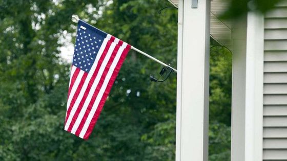 An american flag is hanging from a pole on the porch of a house.
