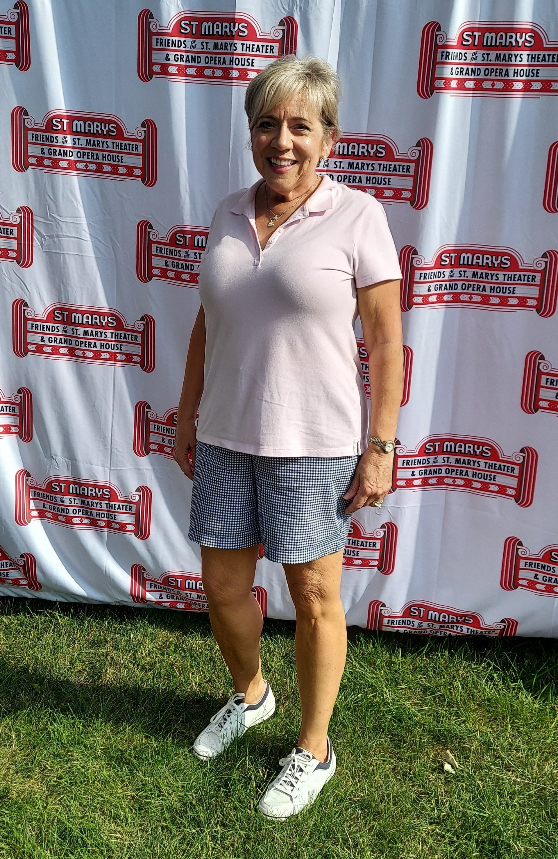 A woman in a pink shirt and shorts is standing in front of a white curtain.
