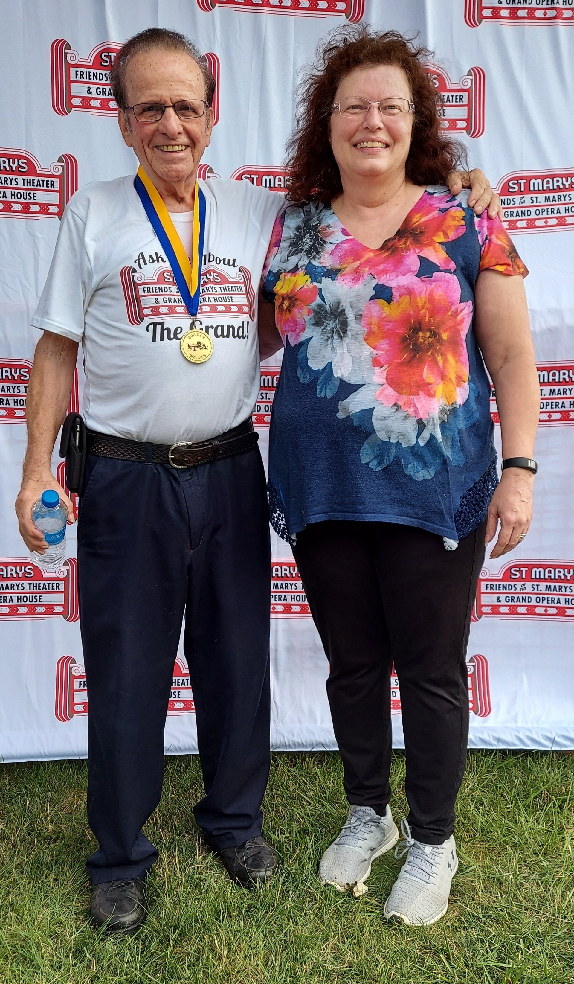 A man and a woman are standing next to each other in front of a white wall.