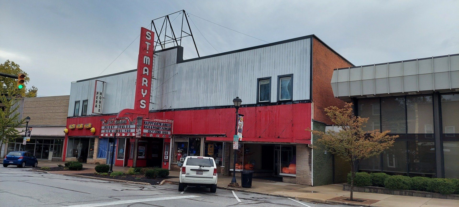 A white suv is parked in front of a large red building.
