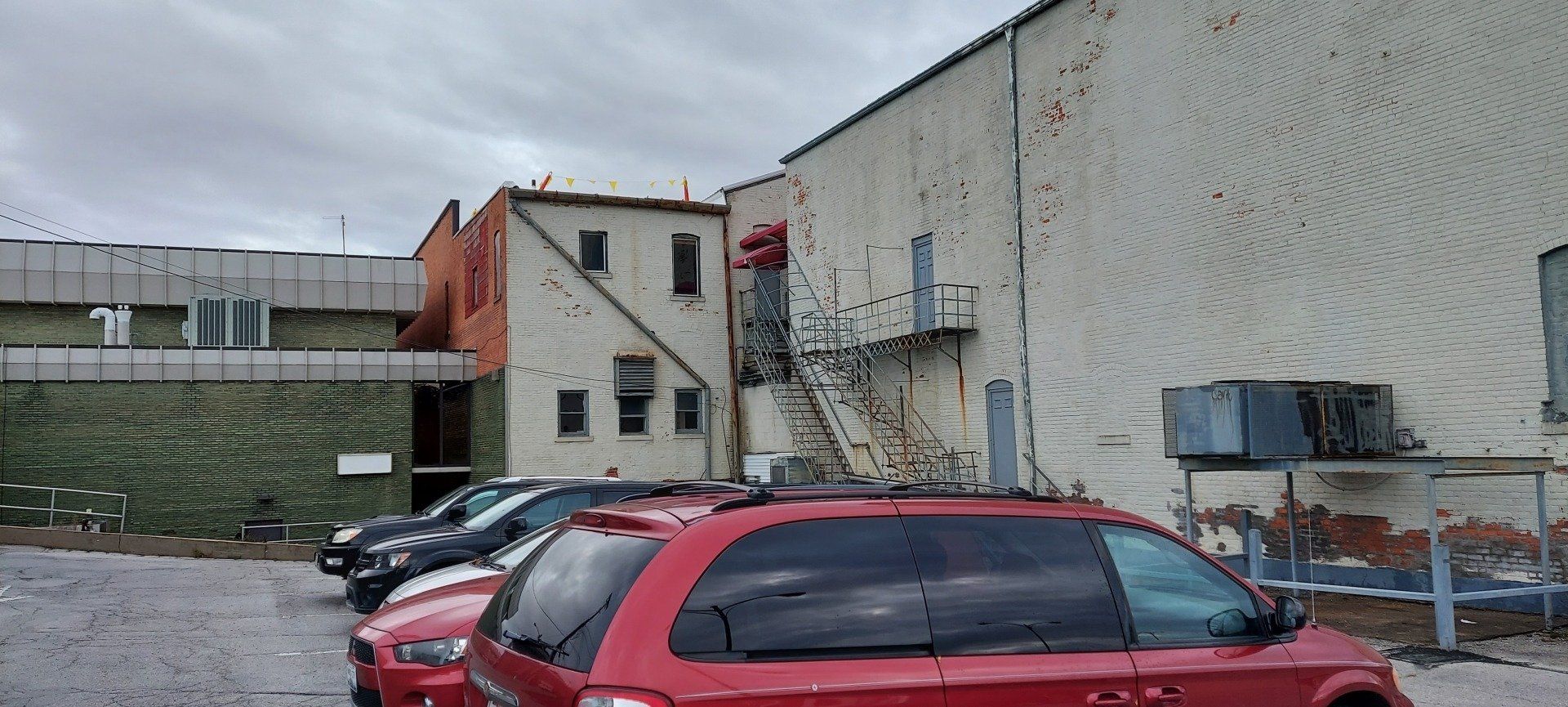 A red car is parked in a parking lot in front of a building.
