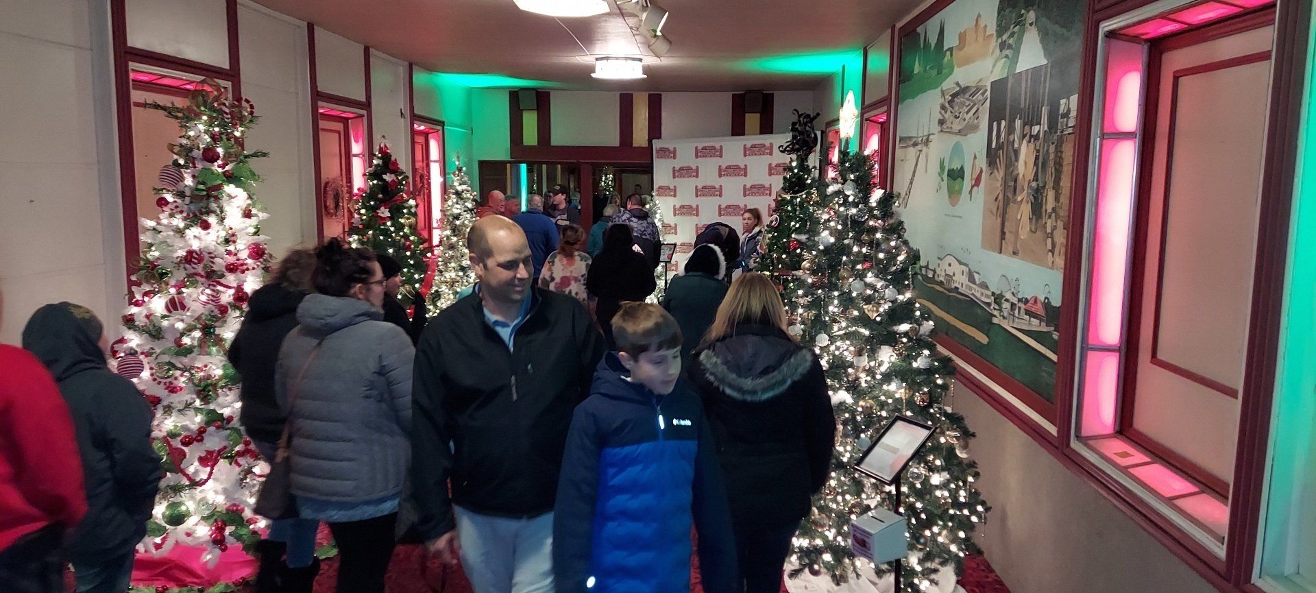 A group of people are walking down a hallway filled with christmas trees.
