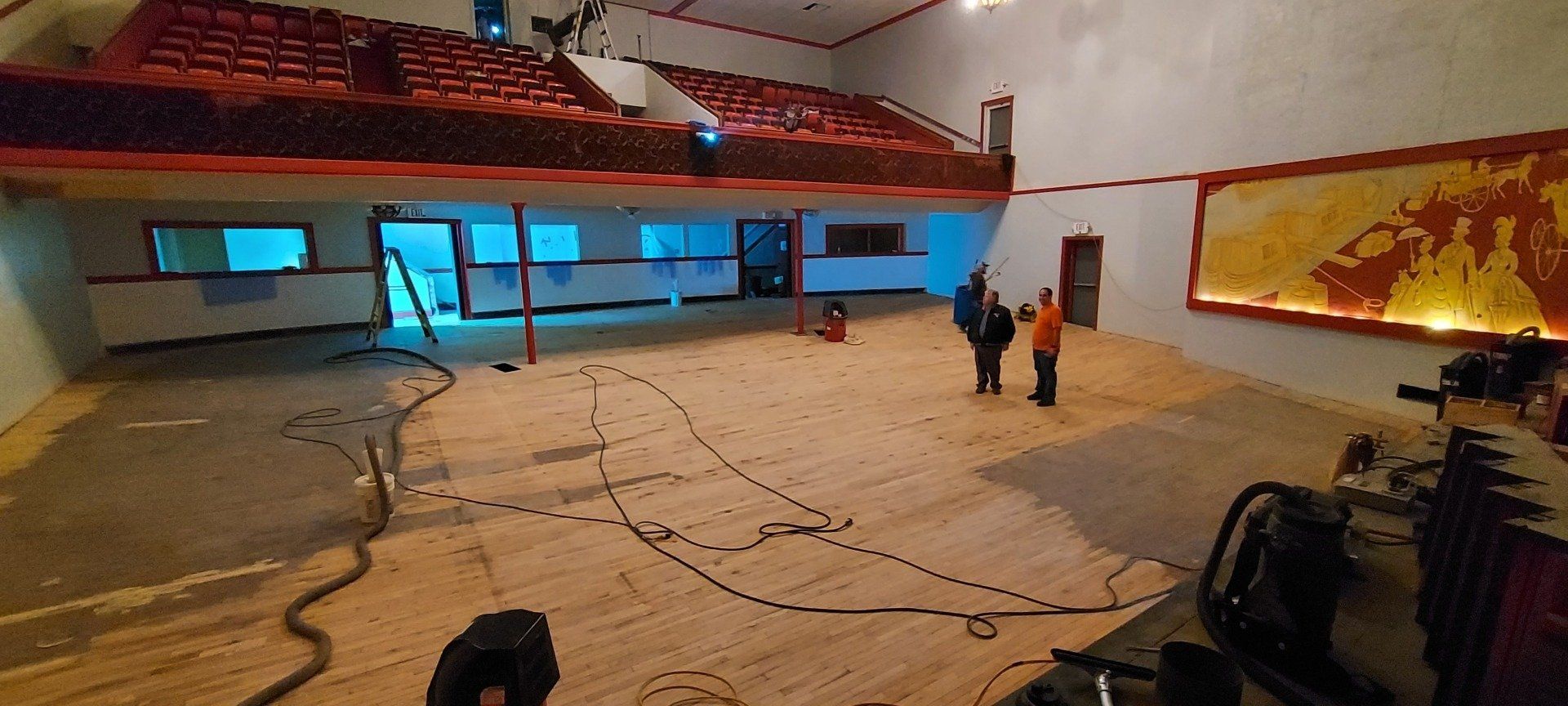 A group of people are standing in a large room with a wooden floor.