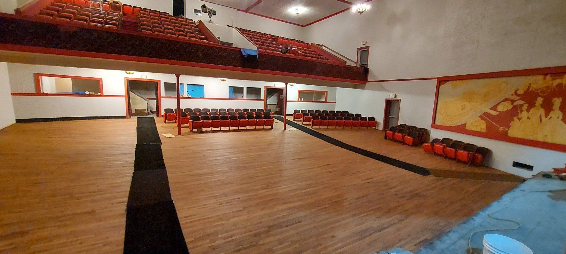 An empty auditorium with wooden floors and red seats