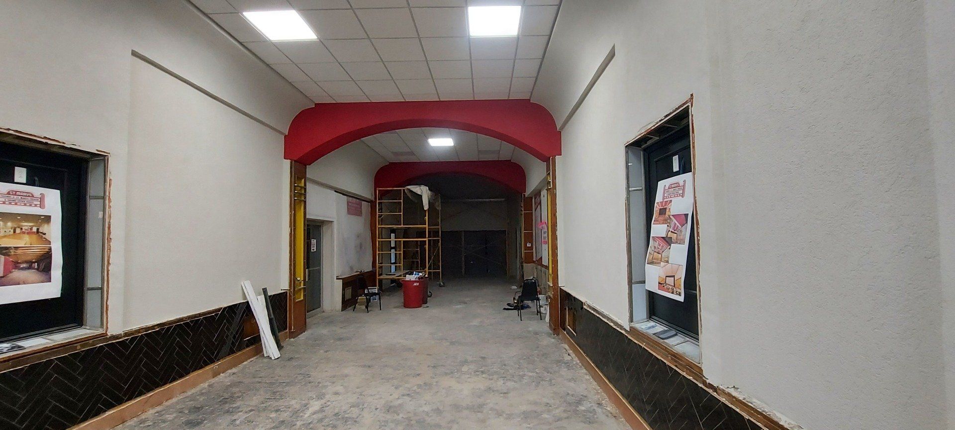 A long hallway with a red archway and a few windows.