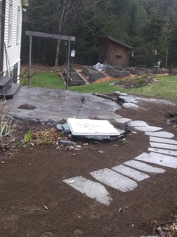 A backyard with a patio, stone pathway, garden beds, and shed.