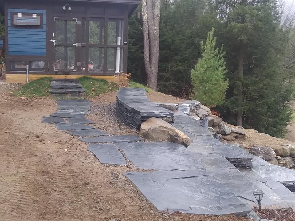 Stone walkway leading to a blue building with glass doors, set on a hillside.