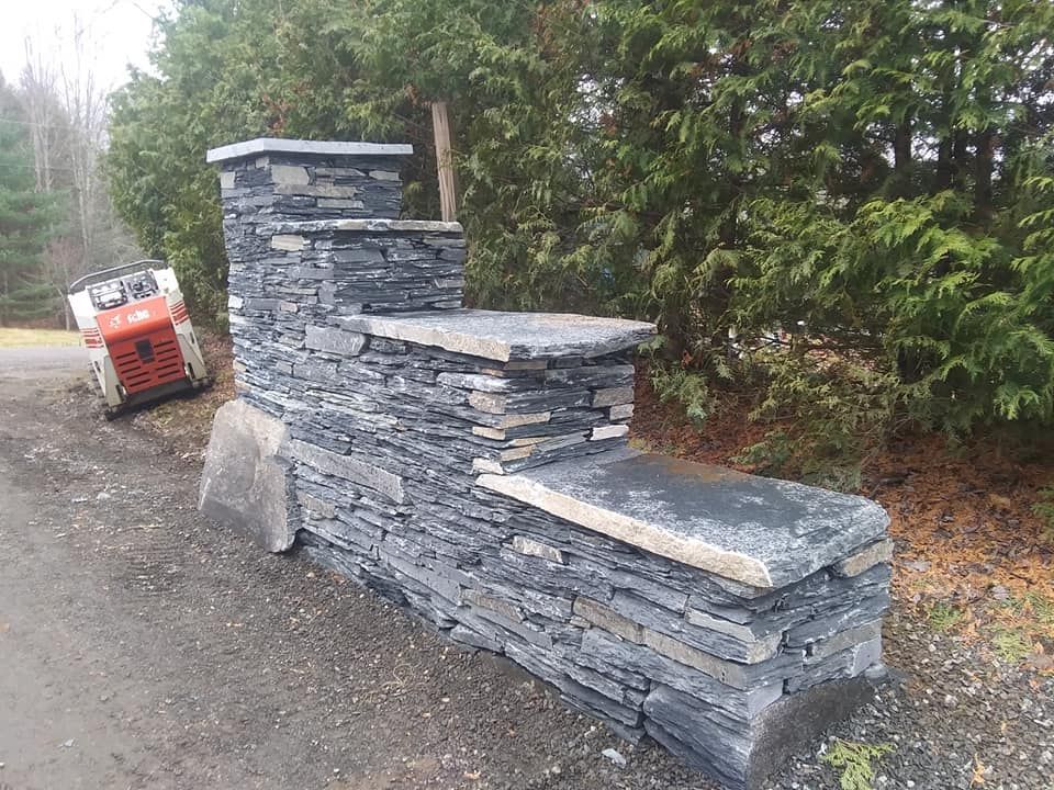 Stone entrance pillar with steps; small construction vehicle in the background.