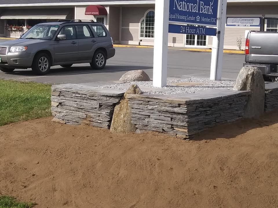 Stone wall base for a sign in front of a bank with a car parked nearby.