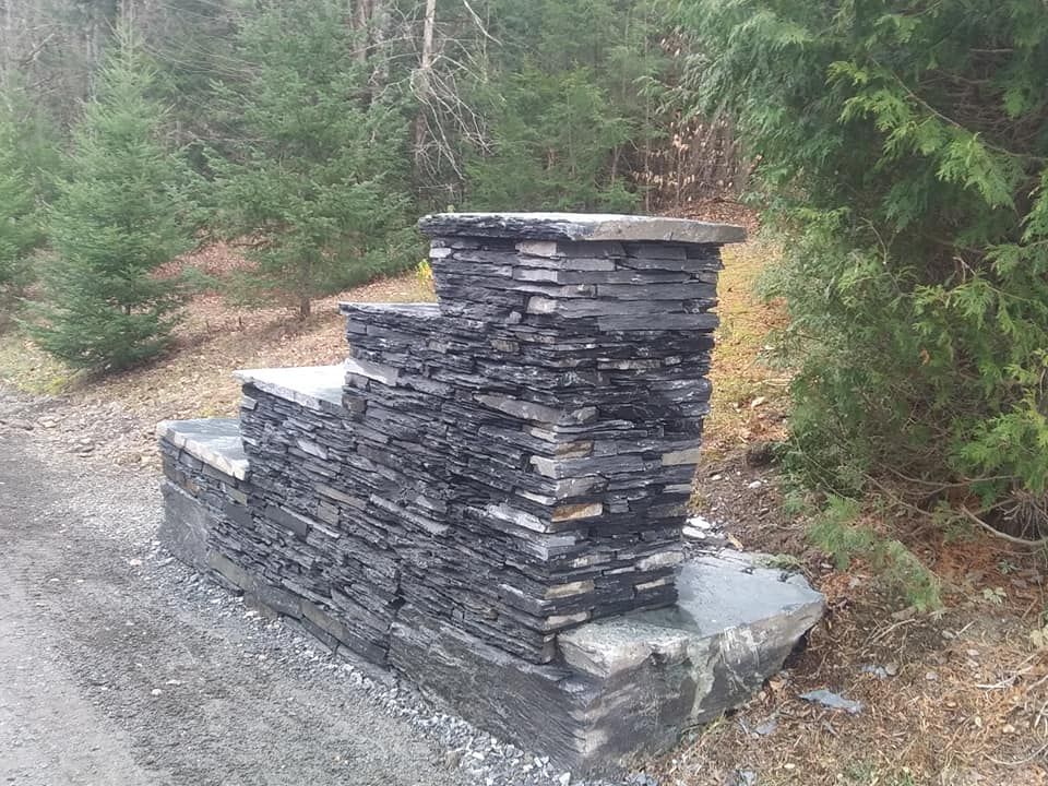 Stone layered mailbox with three tiers in a wooded area.