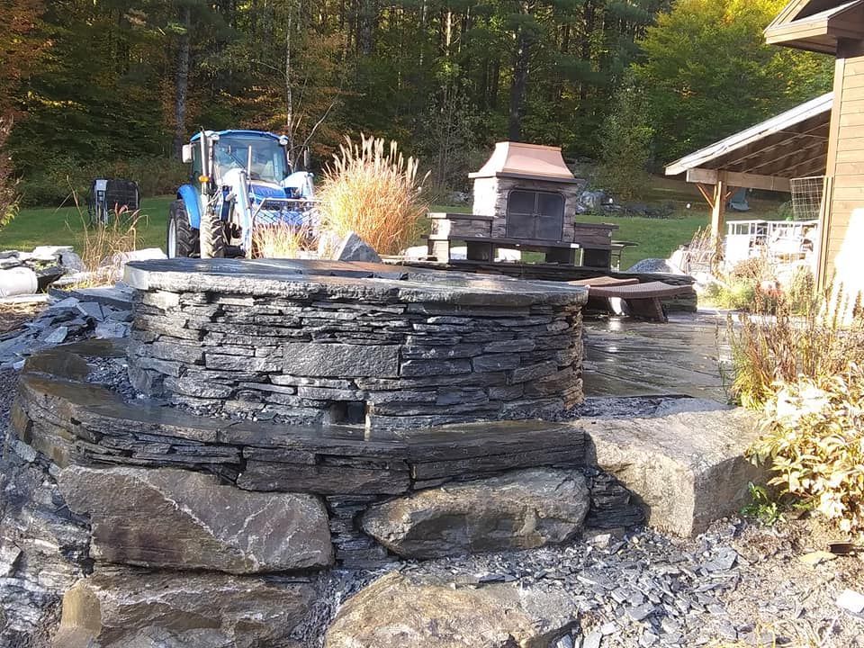 Stone fire pit with a tractor in a grassy outdoor setting.