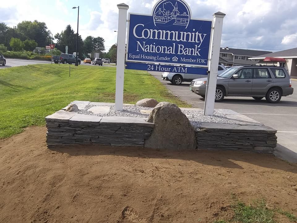 Community National Bank sign with stone base; vehicles and street in background.